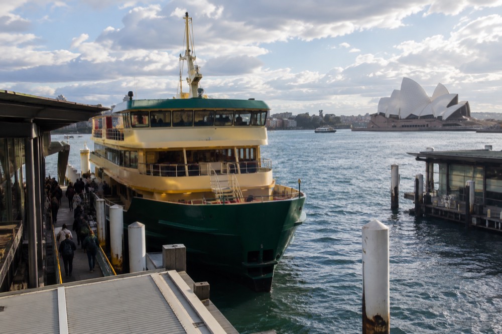A green and yellow Sydney ferry at a Circular Quay wharf with passengers boarding
