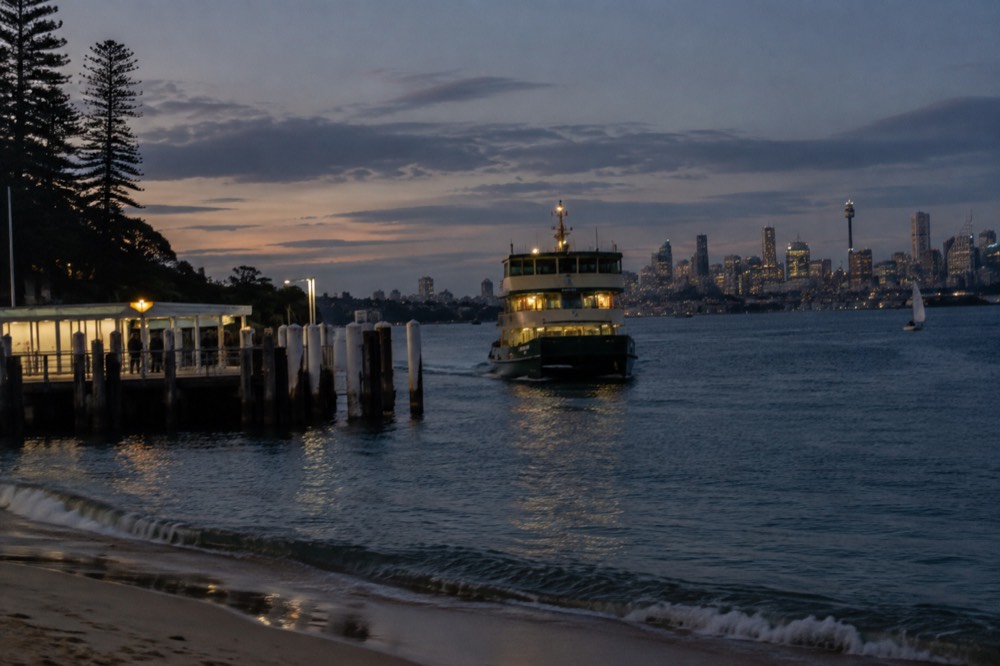 The Manly ferry approaching a wharf with the Sydney skyline across the water in the background