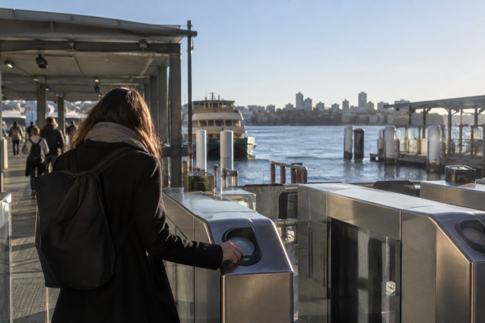 A commuter tapping a contactless card on an Opal reader at a Sydney train station gate
