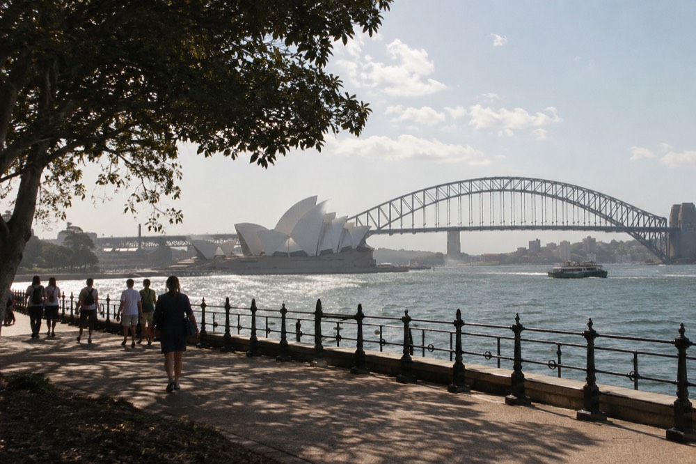 The Sydney Opera House forecourt with the harbour bridge behind it on a clear afternoon