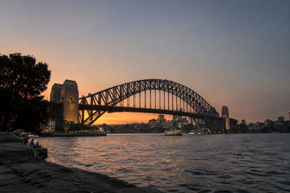 The steel arches of the Sydney Harbour Bridge rising above the harbour at dusk