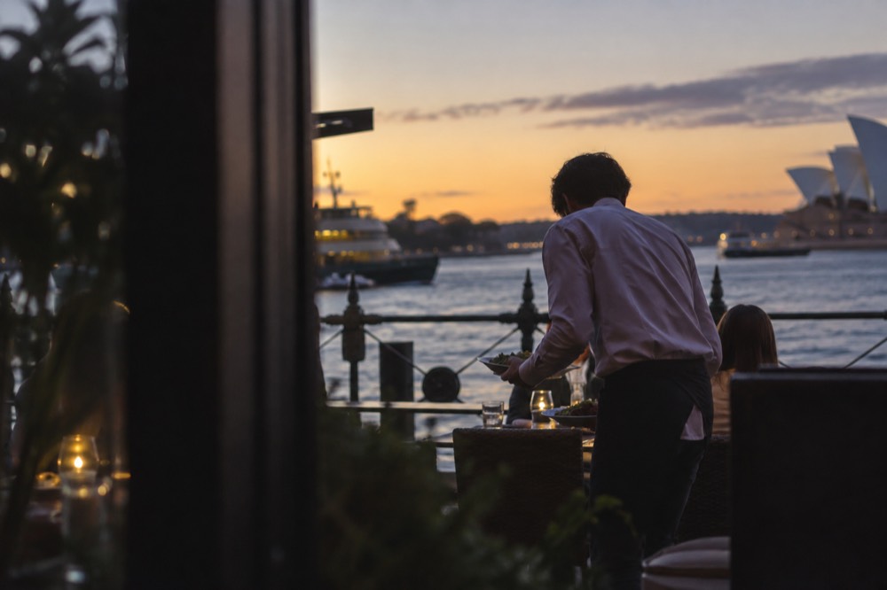 A waiter setting down plates at a small restaurant table in the evening