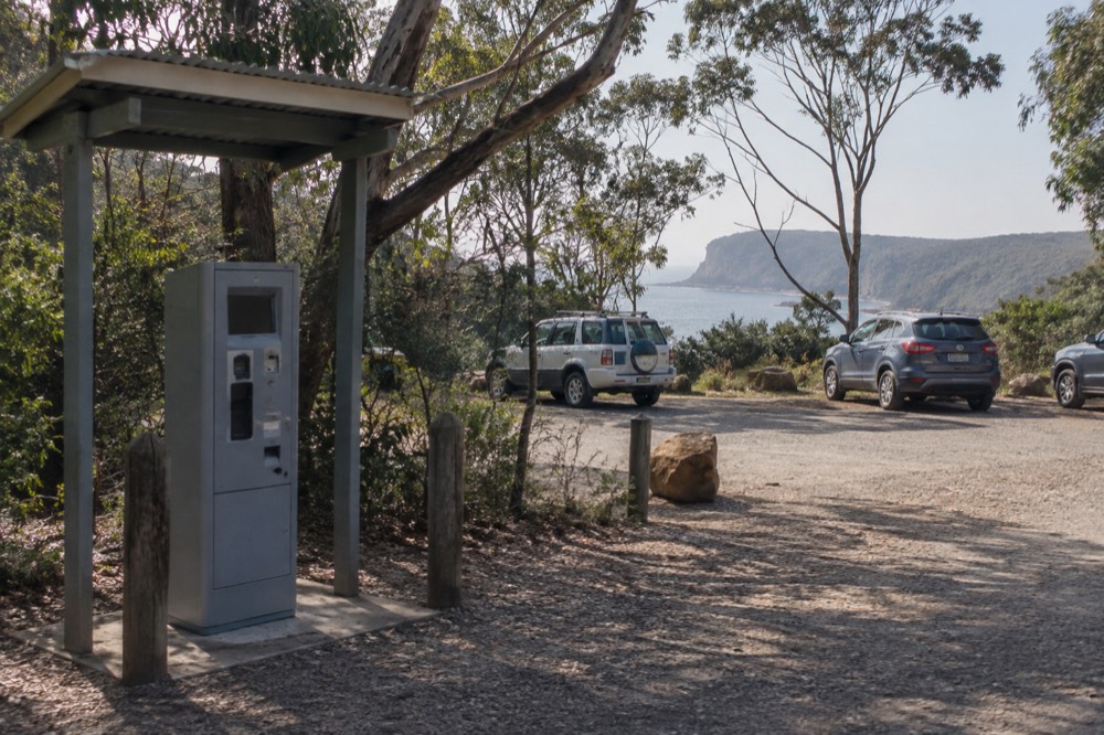 A self-service ticket machine beside a gravel car park surrounded by gum trees