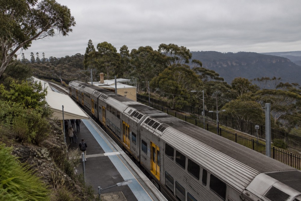 A double-deck train waiting at an elevated Blue Mountains station surrounded by gum trees