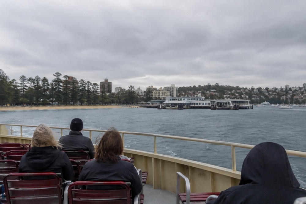 Passengers on the open upper deck of a ferry with Manly Cove and the wharf ahead