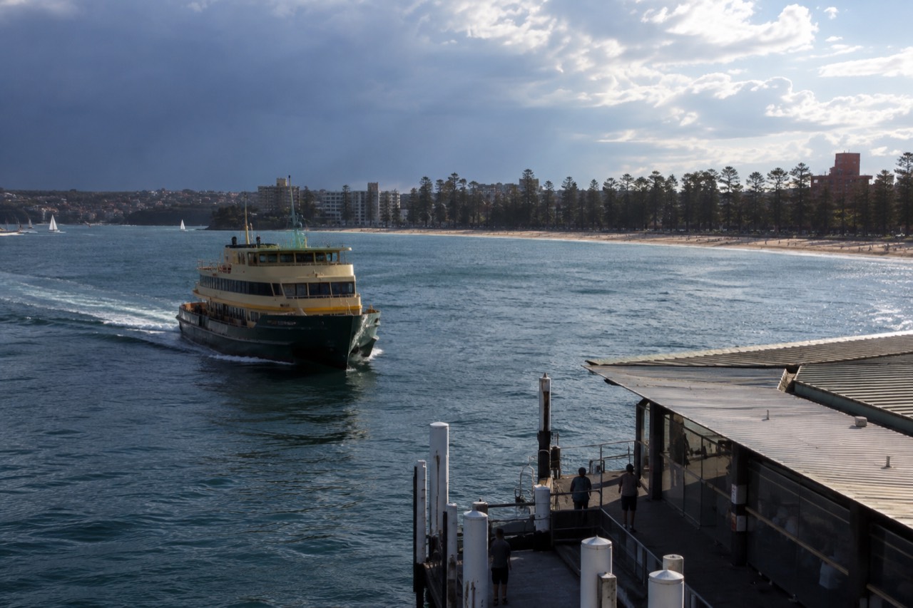 A green and yellow Sydney ferry approaching Manly Wharf across open harbour water