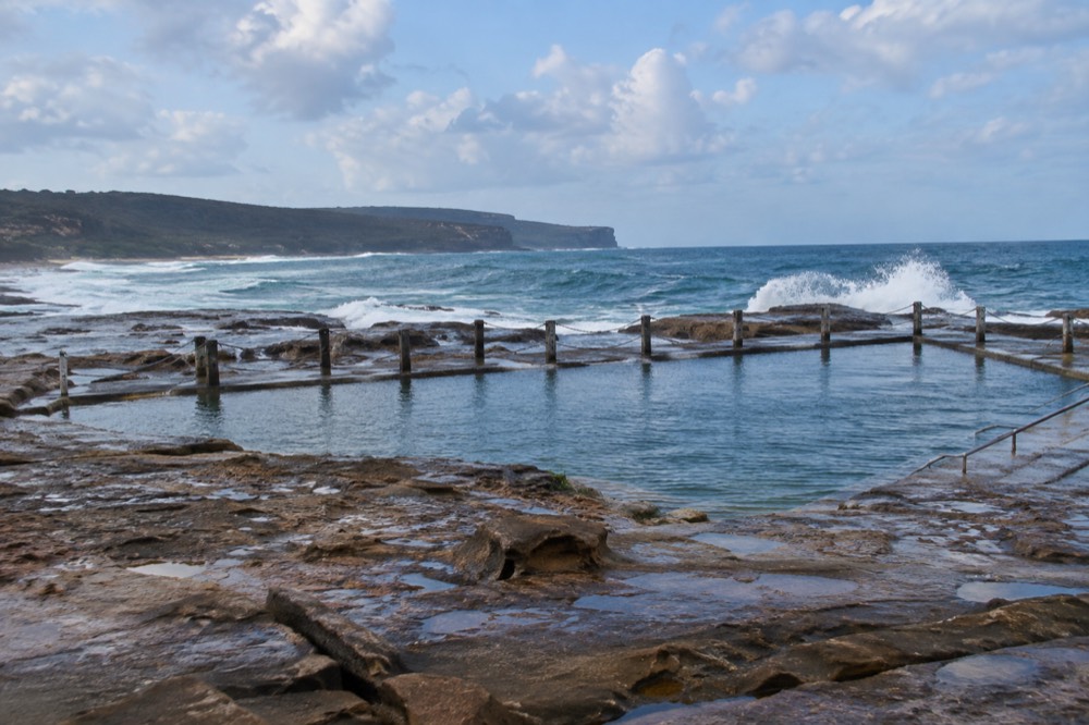 An ocean pool on a rock shelf with waves breaking beyond it at low tide