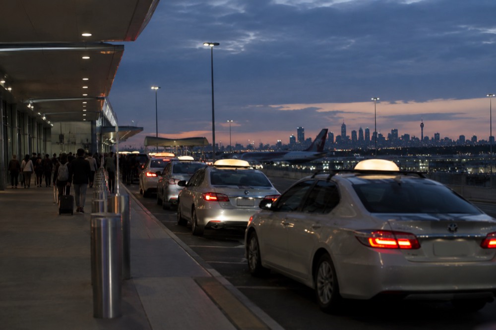 Taxis queued at a kerbside rank outside an airport terminal at dusk