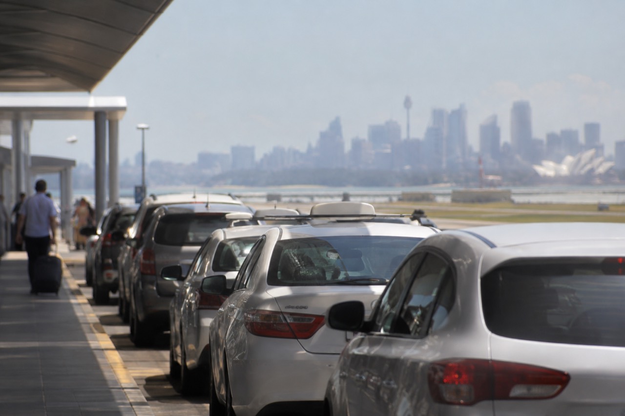 A taxi rank outside the terminal buildings at Sydney Airport with the city skyline in the distance