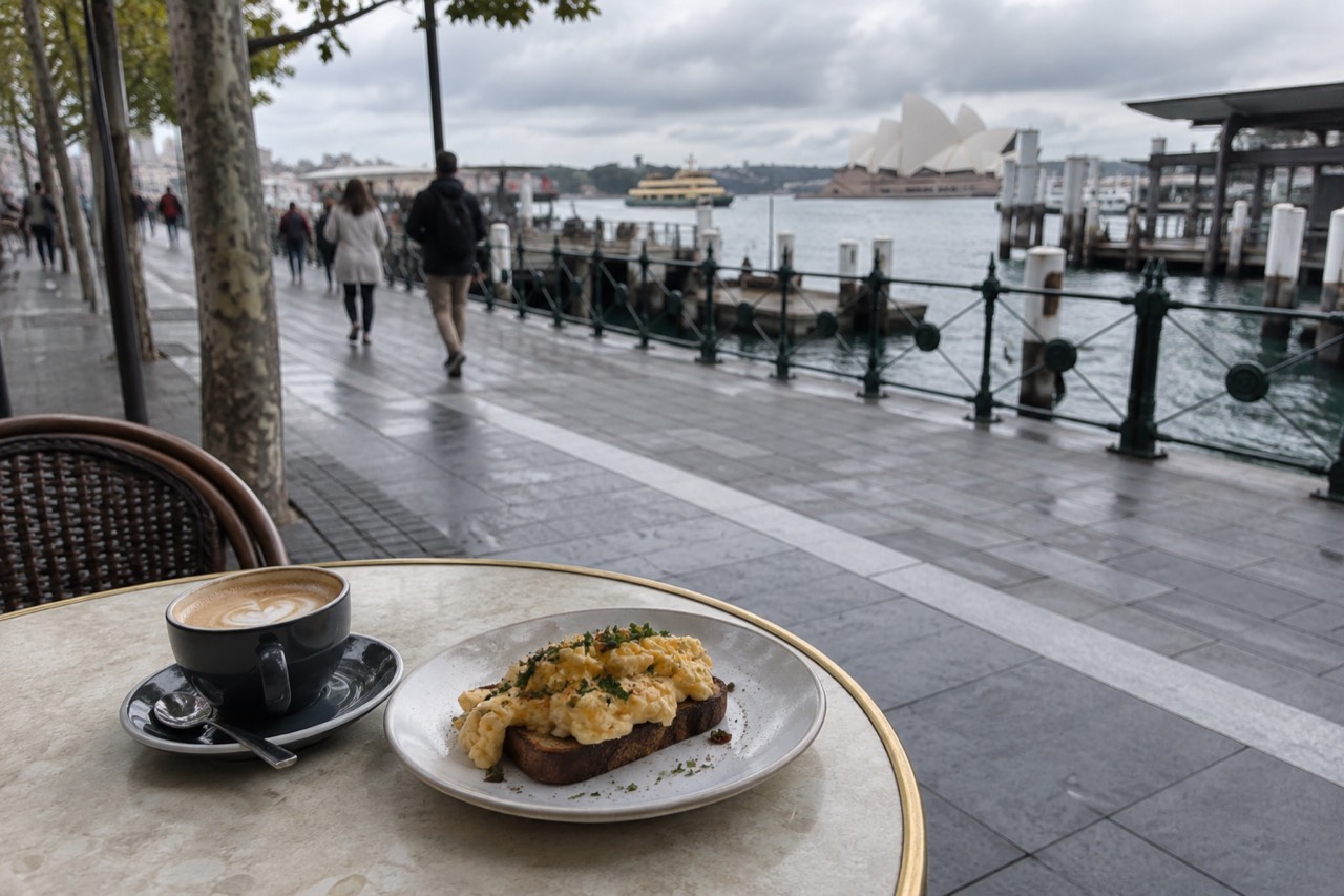 A cafe table beside a Sydney street with a coffee cup and a plate of eggs on toast