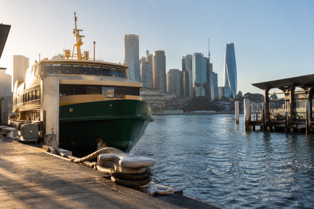 A ferry at a Circular Quay wharf with the city skyline behind it on a clear morning