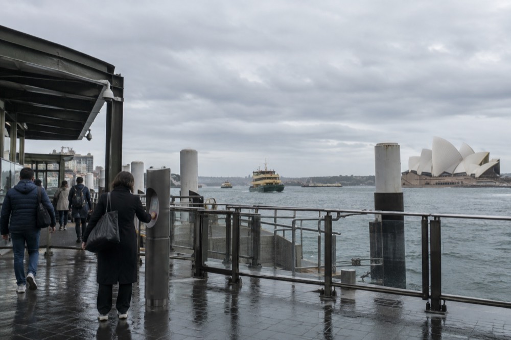 Commuters tapping on at an Opal card reader beside a ferry wharf