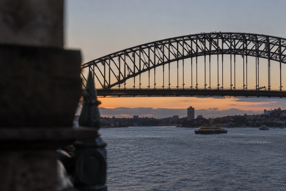 The upper arch of the Sydney Harbour Bridge seen from below with climbers in grey suits on the walkway