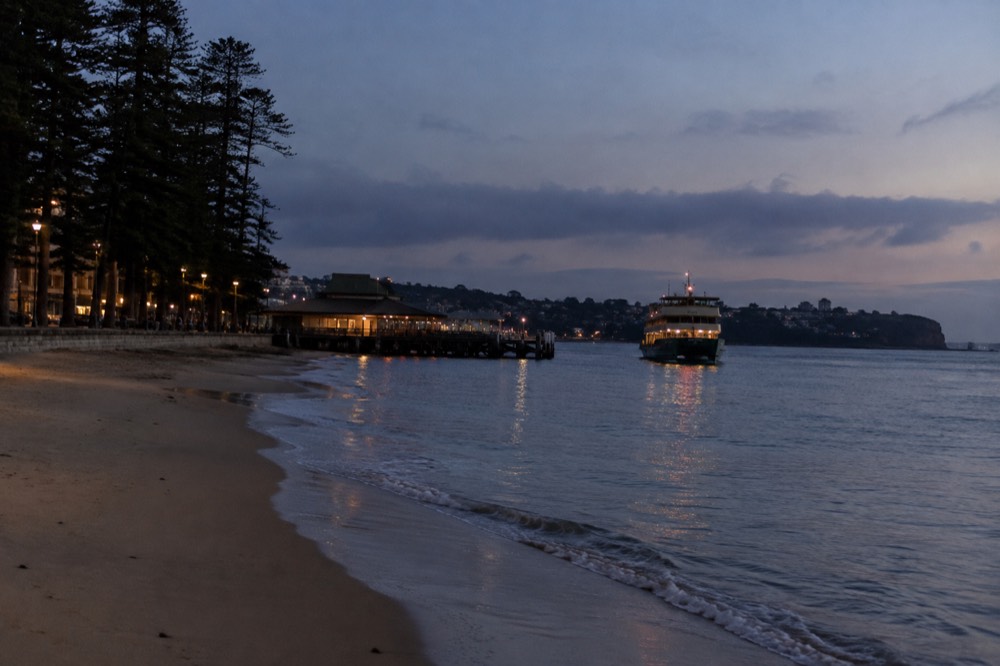 A ferry approaching Manly wharf with calm beach water on either side