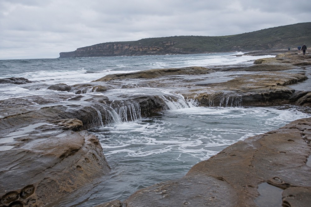 Ocean waves washing over the sandstone rock shelf near the Figure Eight Pools at low tide