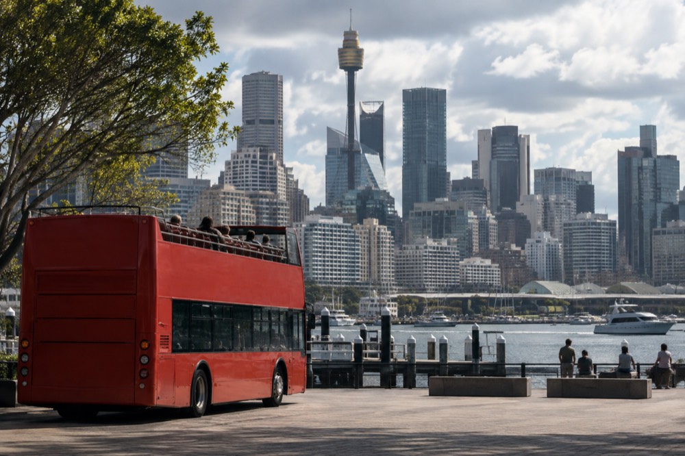 An open-top sightseeing bus parked near Darling Harbour with the city skyline behind it