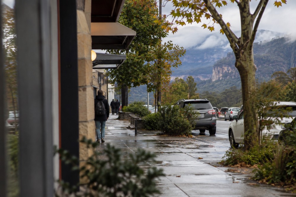 Tree-lined main street of a Blue Mountains village with sandstone shopfronts and mist over the escarpment