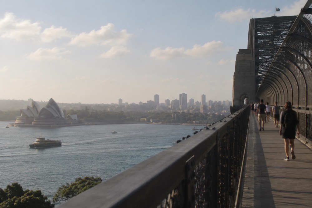 Pedestrians on the eastern walkway of Sydney Harbour Bridge with the Opera House visible across the water