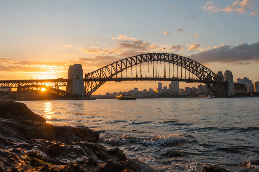 The summit arch of the Harbour Bridge at sunrise, with the city skyline and harbour water glowing in early light