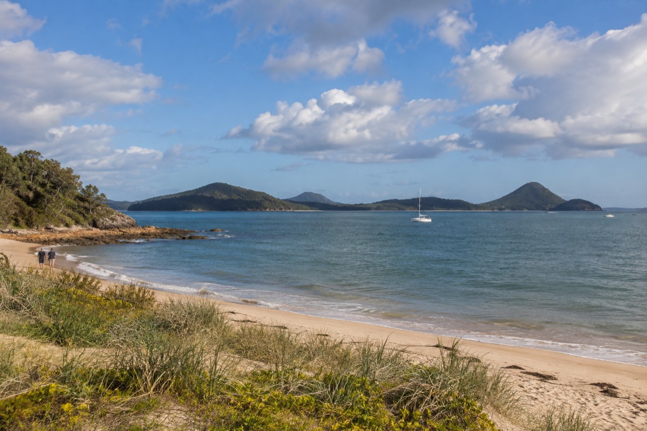 Calm blue bay water with sandy dunes and green headlands under a wide sky