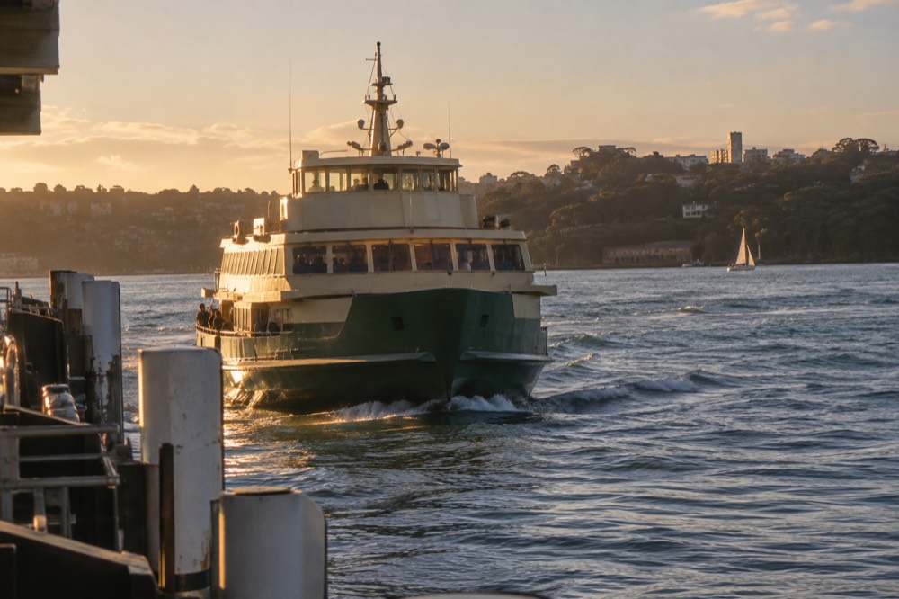 Ferry on Sydney Harbour approaching a wharf with green bushland hillsides