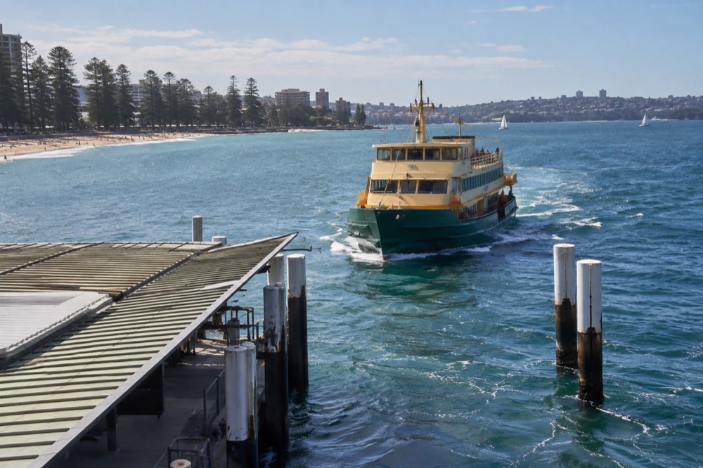 A green and yellow Sydney ferry approaching Manly wharf on open water