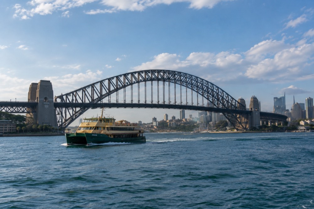 A ferry on blue water with Sydney Harbour Bridge and city towers in the background
