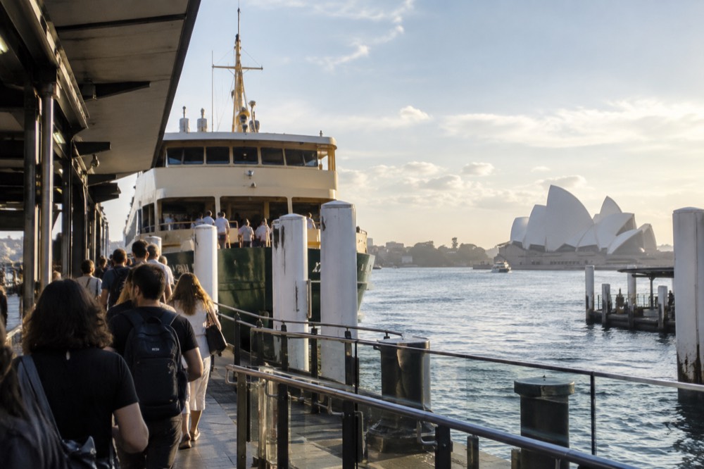 Commuters and visitors boarding a ferry at a Circular Quay wharf in late afternoon light