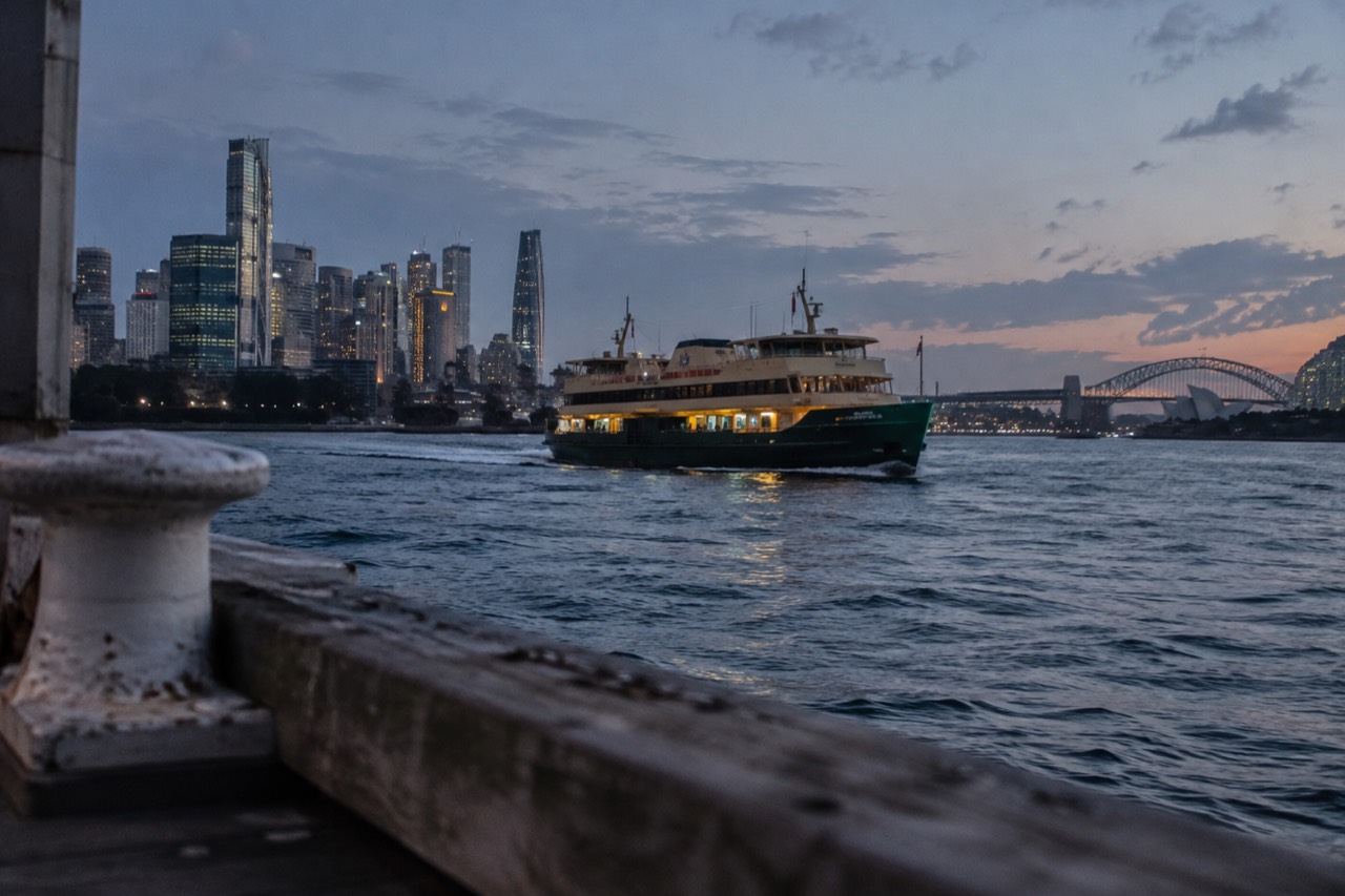 A Sydney ferry crossing open harbour water with distant city towers behind it