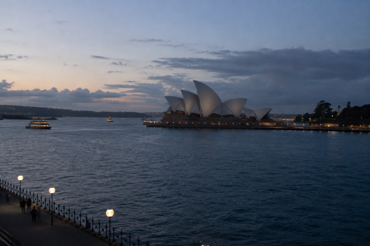The white sails of the Sydney Opera House seen across Circular Quay water at dusk