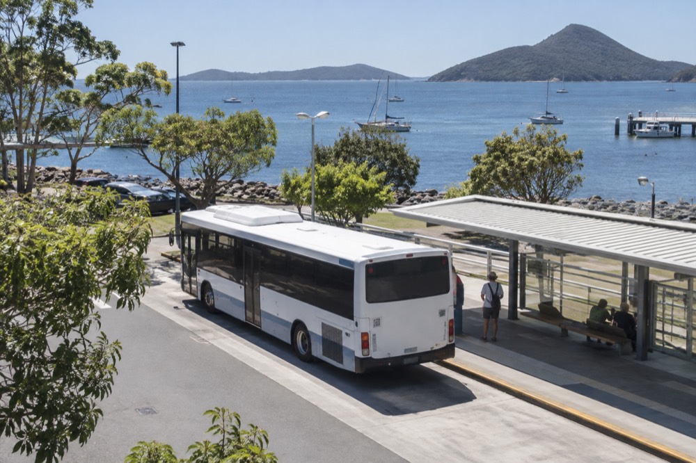 A regional bus parked at a transport interchange with a shelter and timetable signage