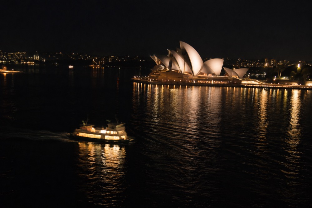 The illuminated Sydney Opera House sails reflected in harbour water at night