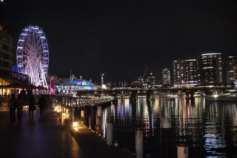 Illuminated ferris wheel and light installations glowing across Darling Harbour at night