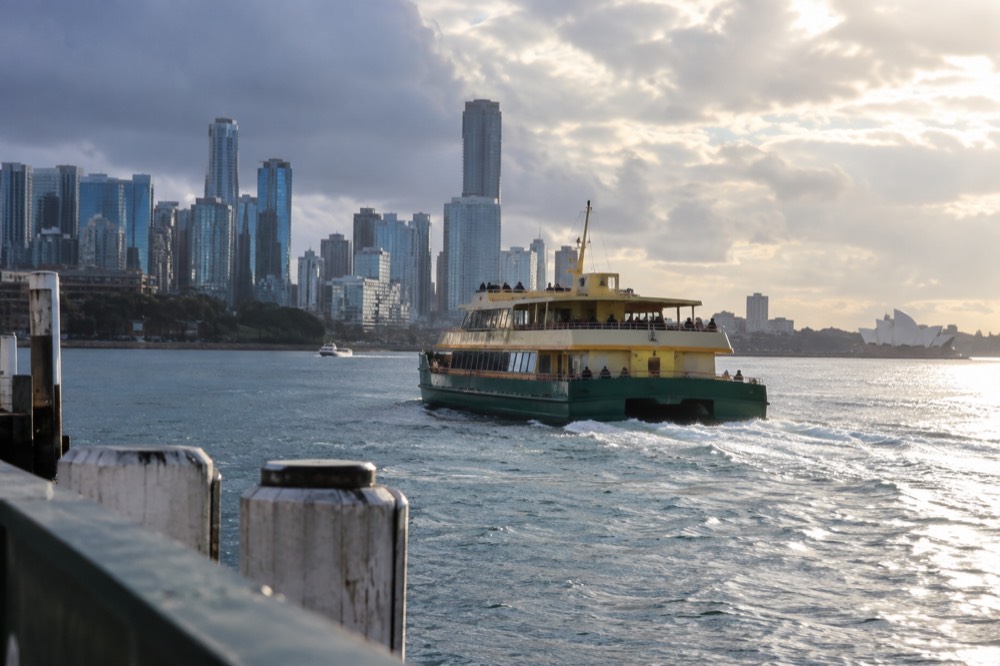 A yellow-and-green Sydney ferry crossing the harbour with the city skyline behind it