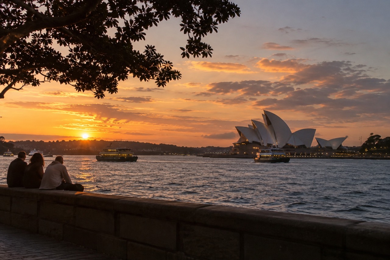 Sydney Harbour at dusk with the Opera House sails and ferry lights on dark water