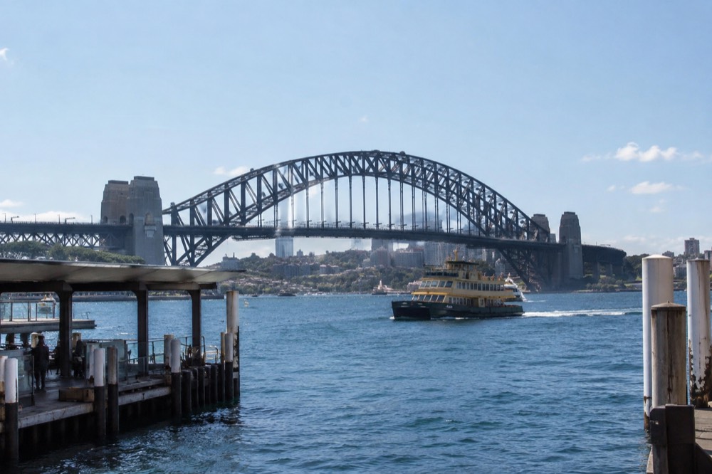 Sydney Harbour Bridge and ferry on blue water seen from a Circular Quay wharf