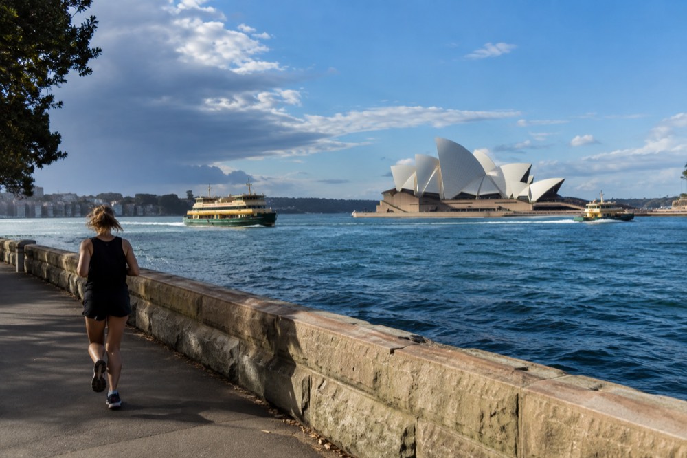 Sydney Opera House sails against a blue harbour sky with ferry boats on the water