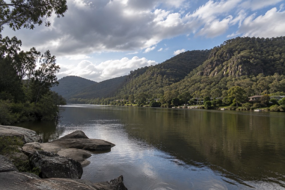 A calm river winding between forested sandstone hills with a small waterside settlement on the bank