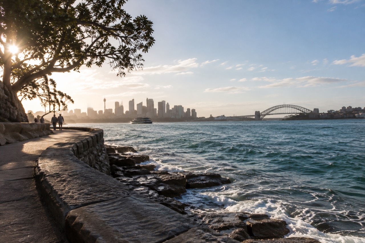 A sandstone coastal path curving above turquoise water with waves breaking on rocks below