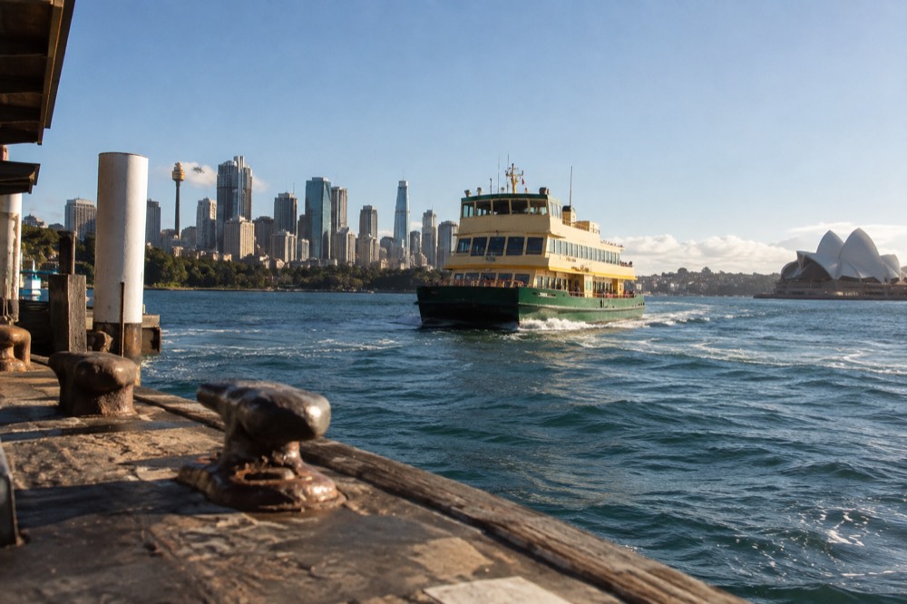 A green and yellow Sydney ferry crossing the harbour toward the city skyline
