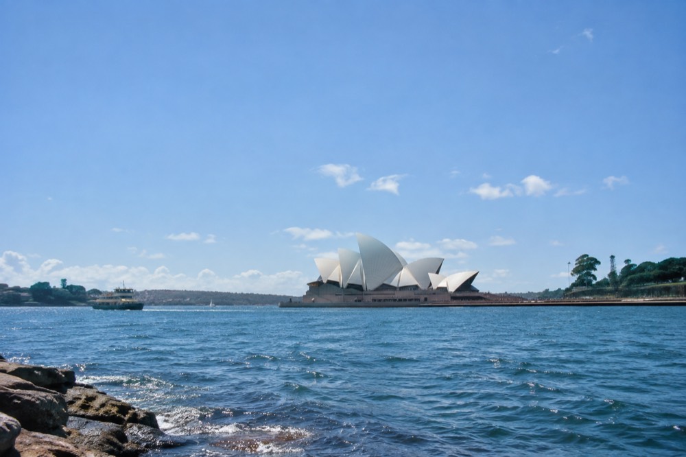 Sunlit Sydney harbour foreshore with the Opera House sails against a bright blue summer sky