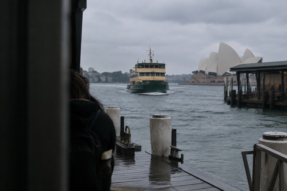 A wooden ferry wharf with a green and yellow ferry approaching across open water