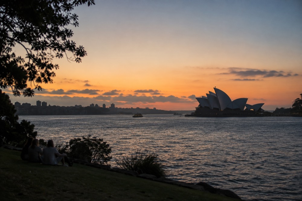 Sydney Opera House sails seen across the water from a harbour foreshore park
