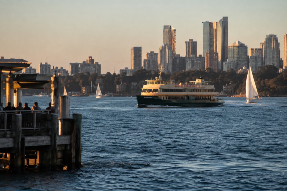 Ferry and sailing boats on open harbour water with city towers behind
