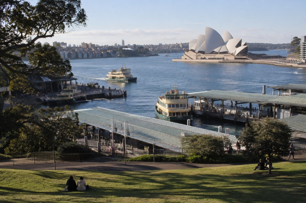 Garden lawns sloping down to a harbour cove with the Opera House in the distance