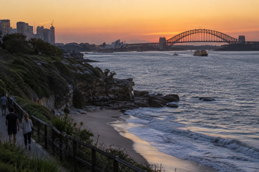A clifftop path above a curved sandy beach with rolling surf