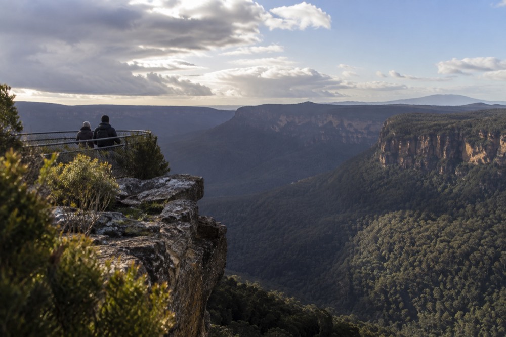 Sandstone cliffs and forested valley in the Blue Mountains under a wide sky
