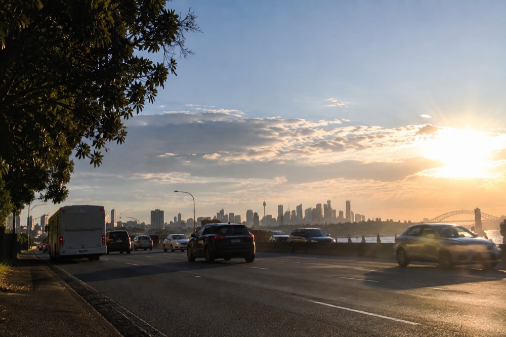 Buses and cars moving through a wide Sydney road corridor near the airport with city towers in the distance