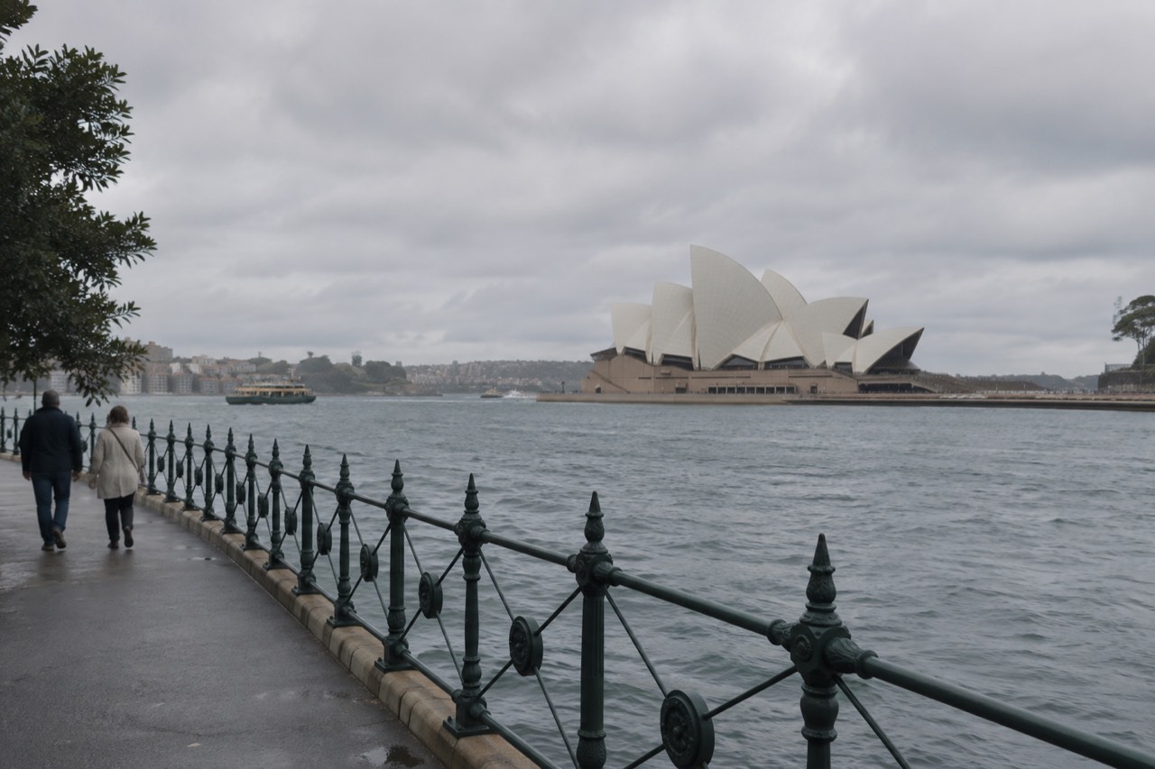 Sydney Opera House sails seen across the water from a harbour walkway at mid-morning