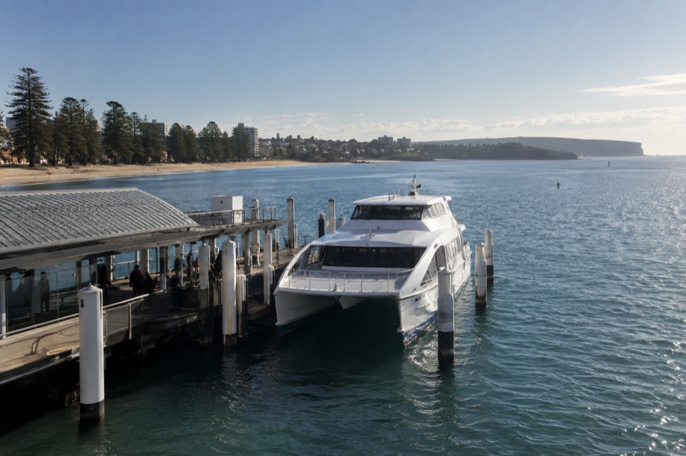 A sleek private catamaran ferry moored at a Manly wharf on a clear morning